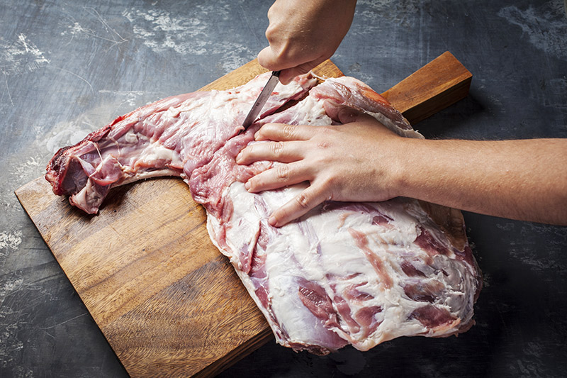 After having identified the first four ribs attached to the neck, turn the rack back over once again and starting at the neck, carefully slice downwards following the line of the neck and the first rib closest to the neck.